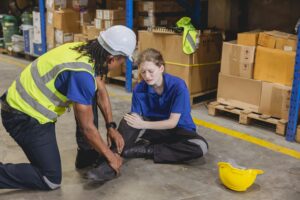 young woman warehouse worker accident leg injury slip and fall ankle sprain friend help support, health and safety near me