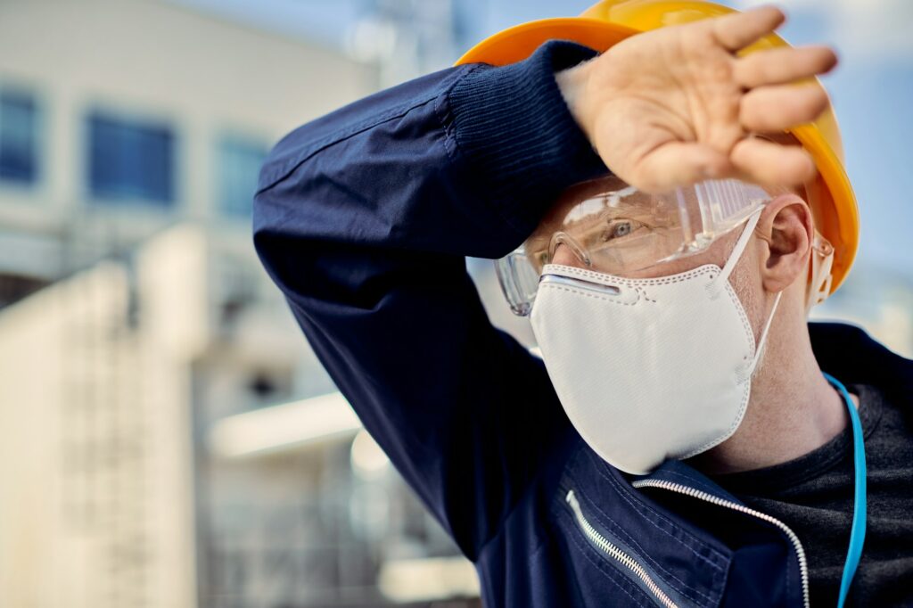 Exhausted civil engineer with protective face mask at construction site.
